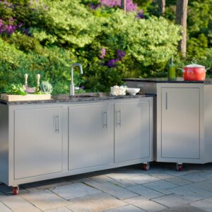 Stainless steel mobile outdoor kitchen with built-in sink and granite prep counter rolling on red casters in a garden setting.