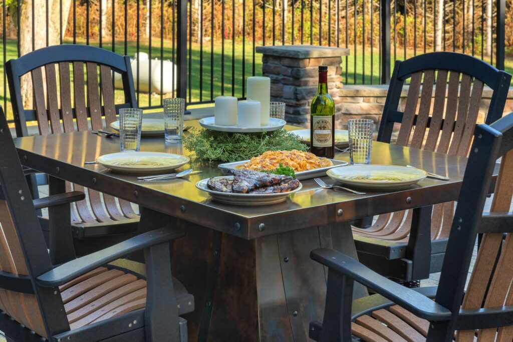 Rocket Outdoors metal patio dining table set with grilled ribs, pasta, wine, and candles for an autumn backyard meal.