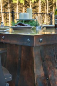 Close-up of the riveted metal top and rich patina edge on a Rocket Outdoors patio dining table set for an evening meal.