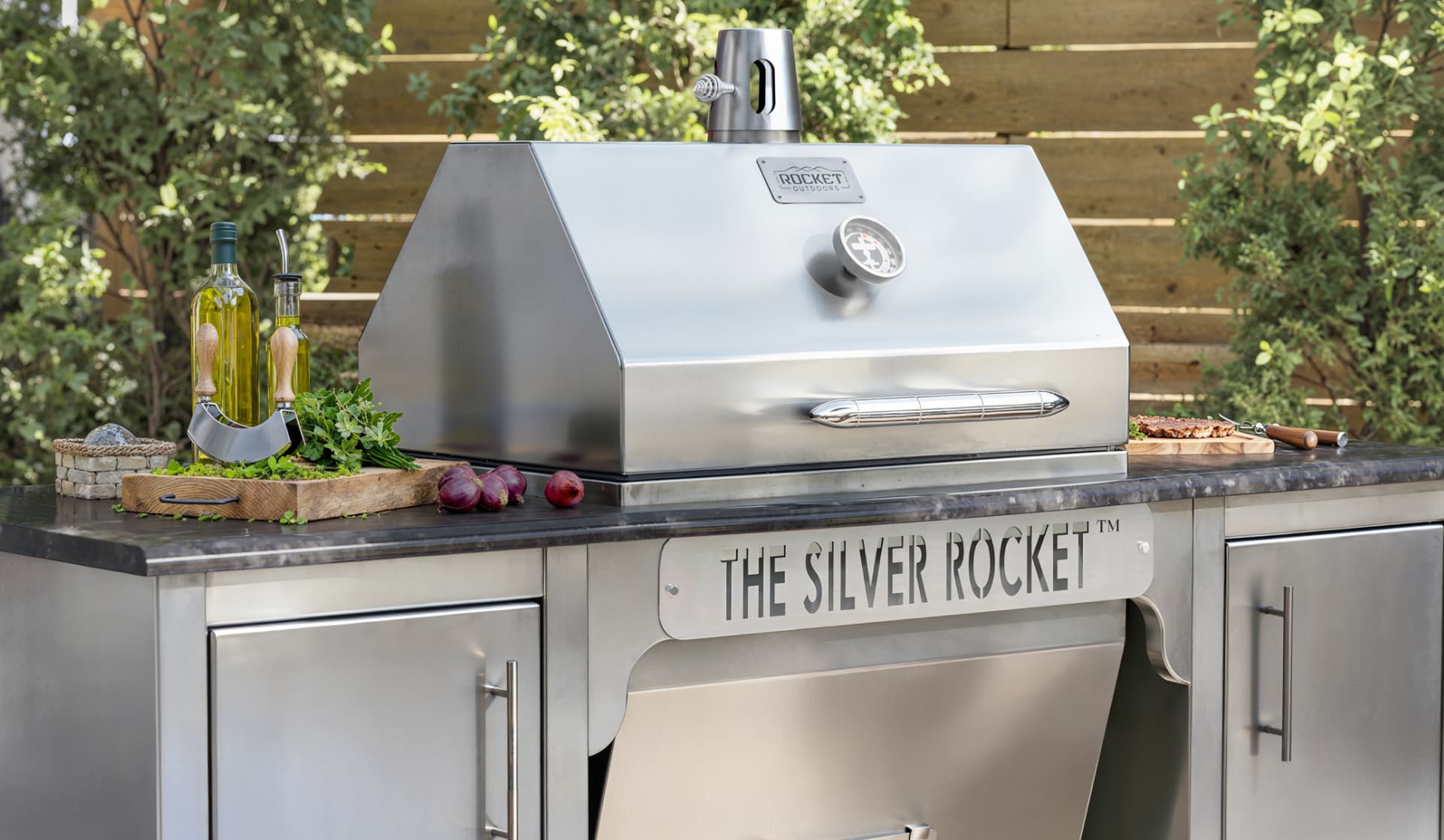 Silver Rocket stainless steel built-in grill installed in a Rocket Outdoors outdoor kitchen with countertop prep space and storage cabinets.