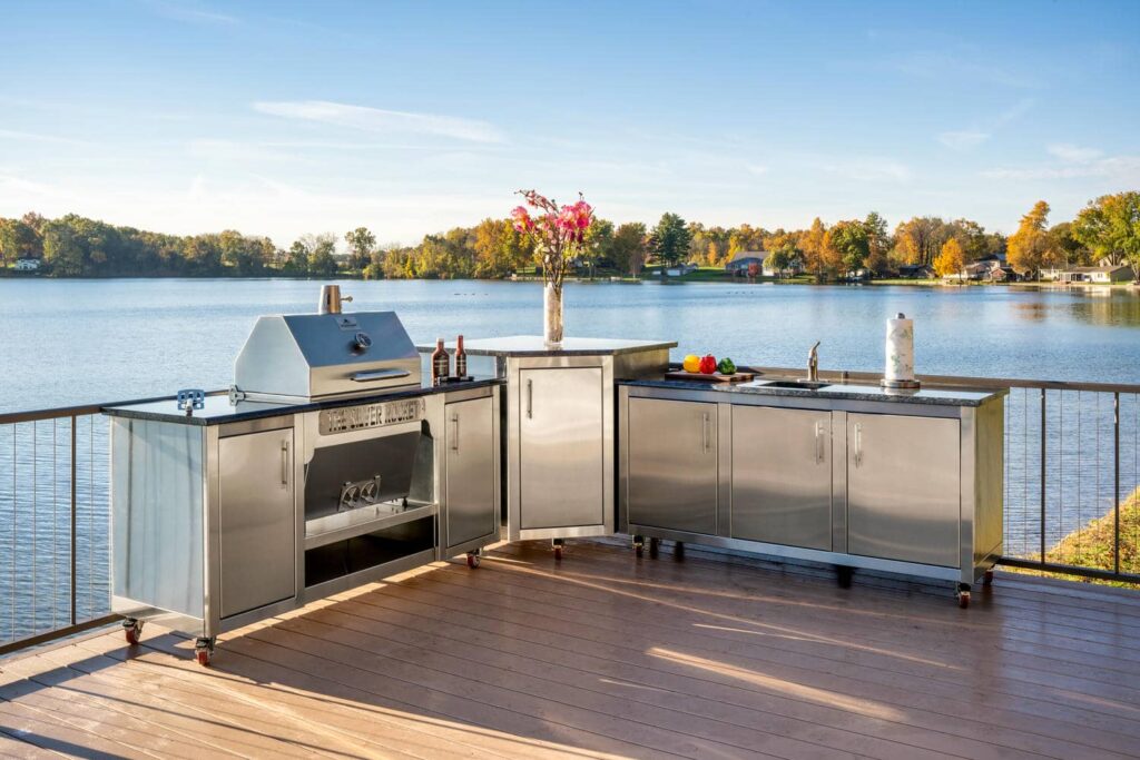 Silver Rocket stainless steel outdoor kitchen with built-in grill and sink on a wooden deck overlooking a lake with autumn foliage.