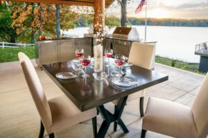 The Silver Rocket built-in outdoor kitchen and stainless dining table set with wine glasses overlooking a lake at sunset.