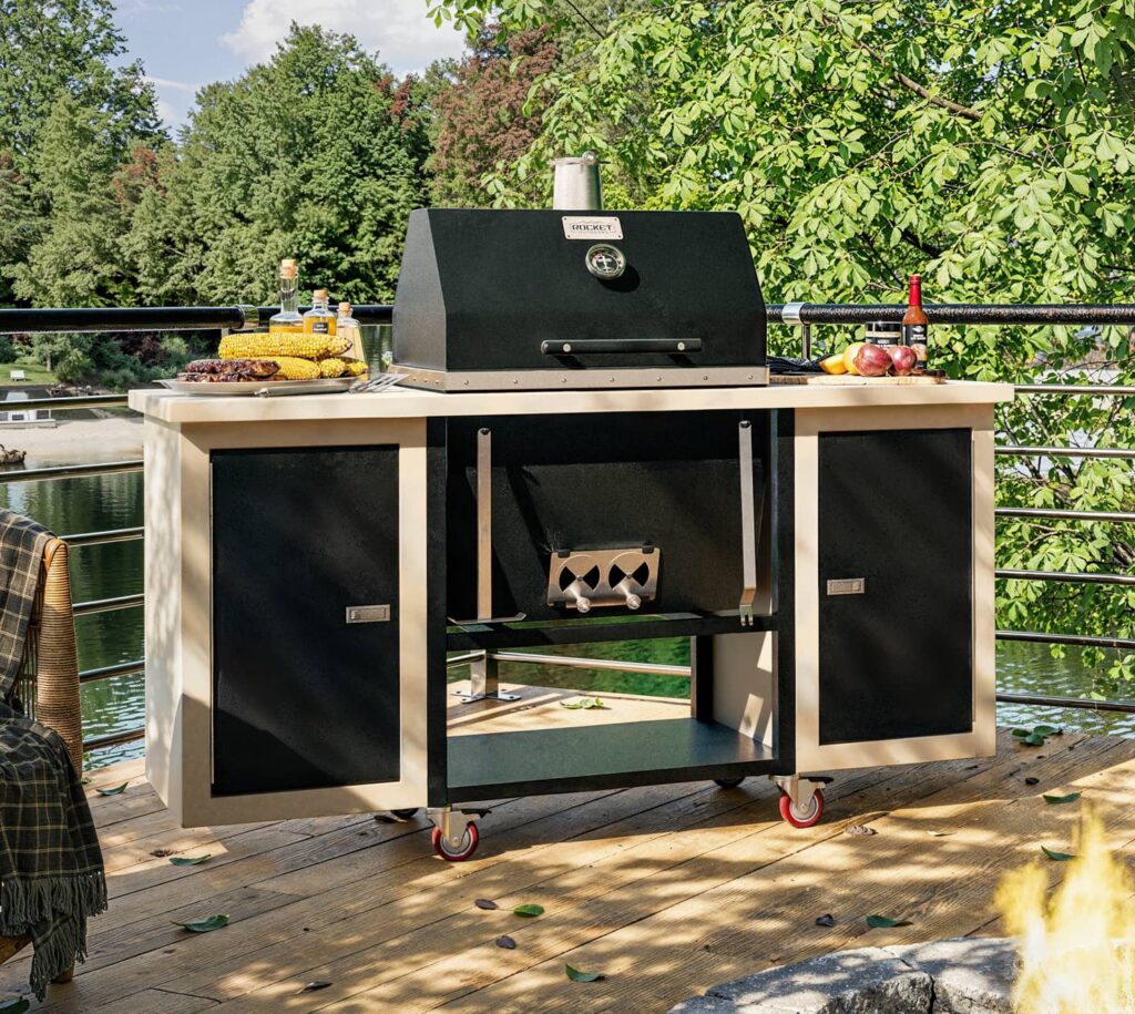 Sonic Rocket charcoal grill on a speckled pearl cart set up on a lakeside deck with grilled corn and peppers ready to cook.