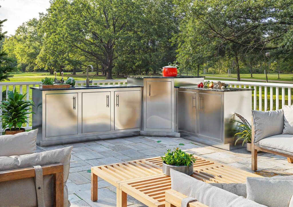 L-shaped Silver Rocket stainless steel outdoor kitchen with sink and prep stations on a stone patio overlooking a park.